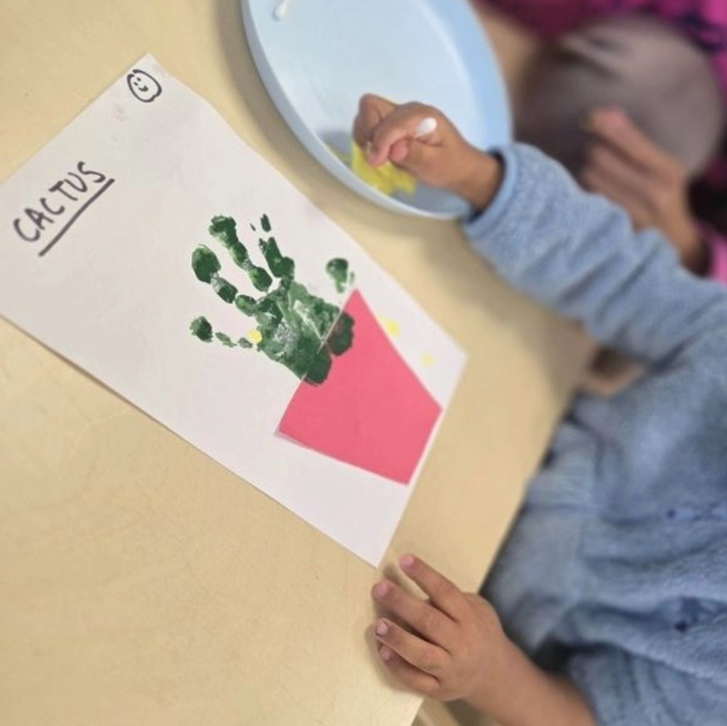 A child's green handprint cactus craft with yellow paint dots